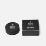 Schwarzer Qualicann Aluminium-Grinder mit Logo, neben der dazugehörigen Verpackung, vor weißem Hintergrund.