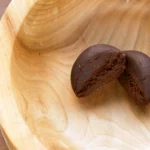 Halbierte Kugel aus weichem CBD-Haschisch in einer Holzschale – braune, gleichmäßige Textur mit feinporigem Innenleben.