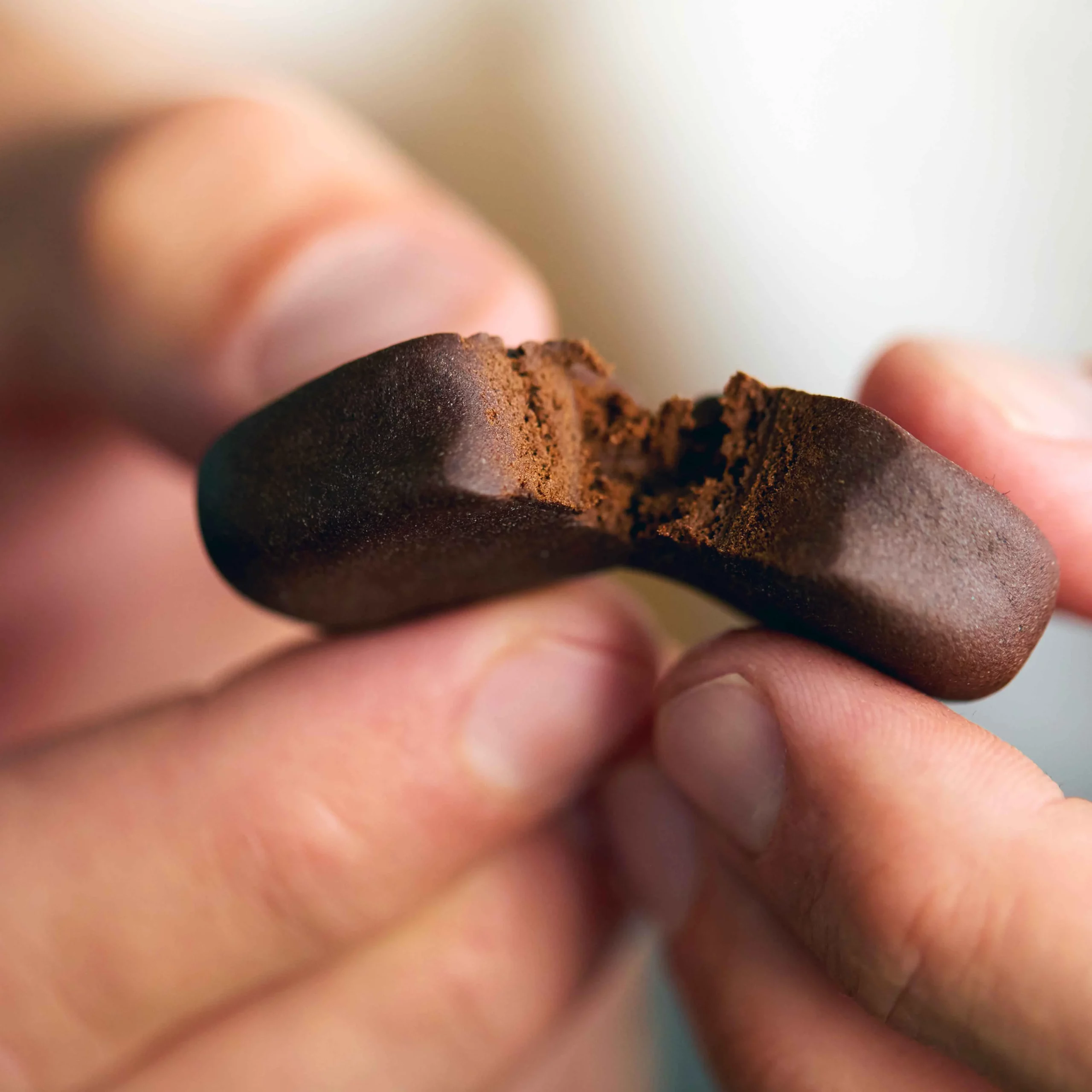 Nahaufnahme zweier Finger, die ein Stück weiches, braunes CBD-Haschisch auseinanderbrechen – feinporige, harzige Textur im Fokus.