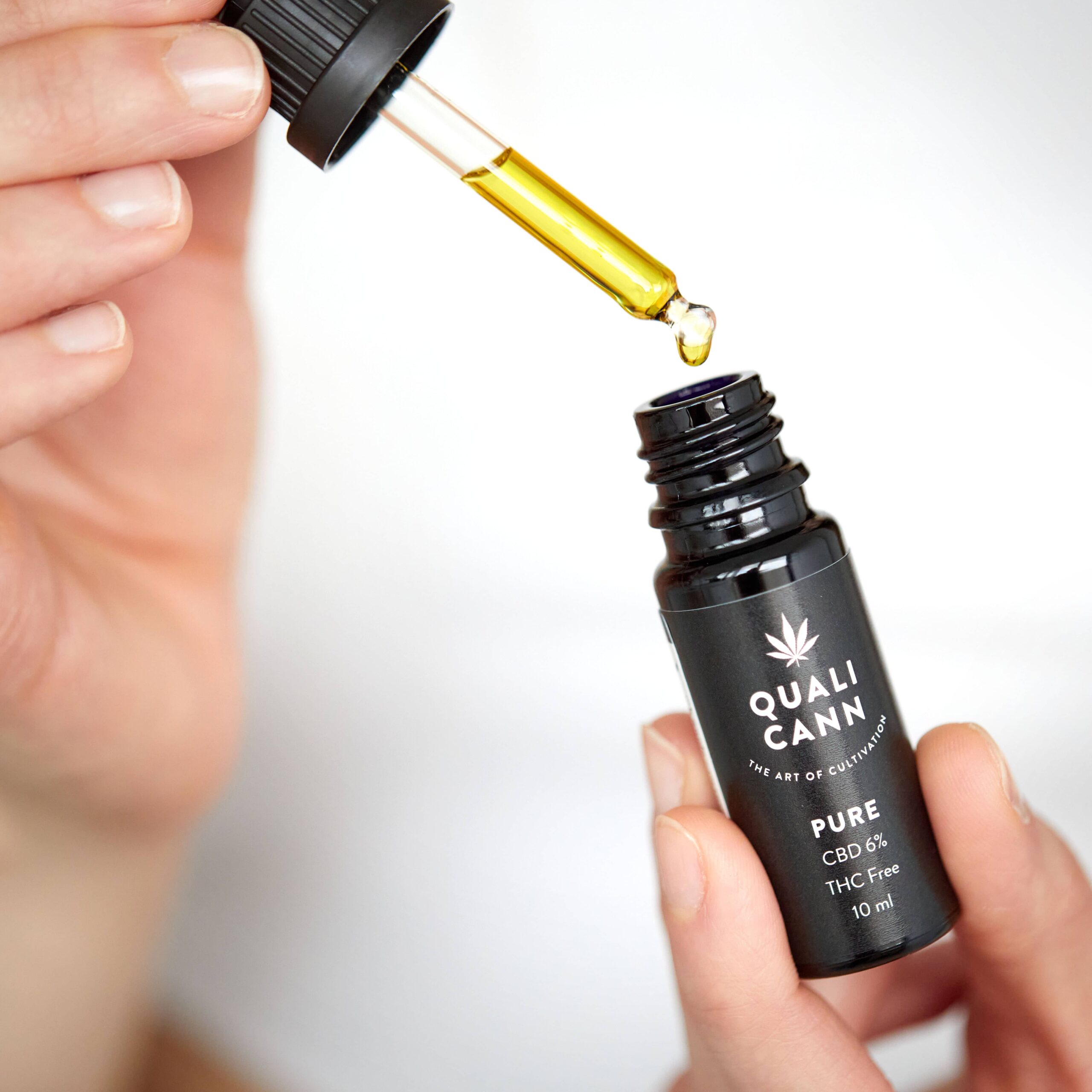 Nahaufnahme einer Hand mit einer Pipette und einer Flasche Qualicann Pure CBD Öl 6 % THC-frei – hochwertiges Schweizer CBD Isolat Öl in Hanfsamen-Basisöl für reine Qualität ohne THC.