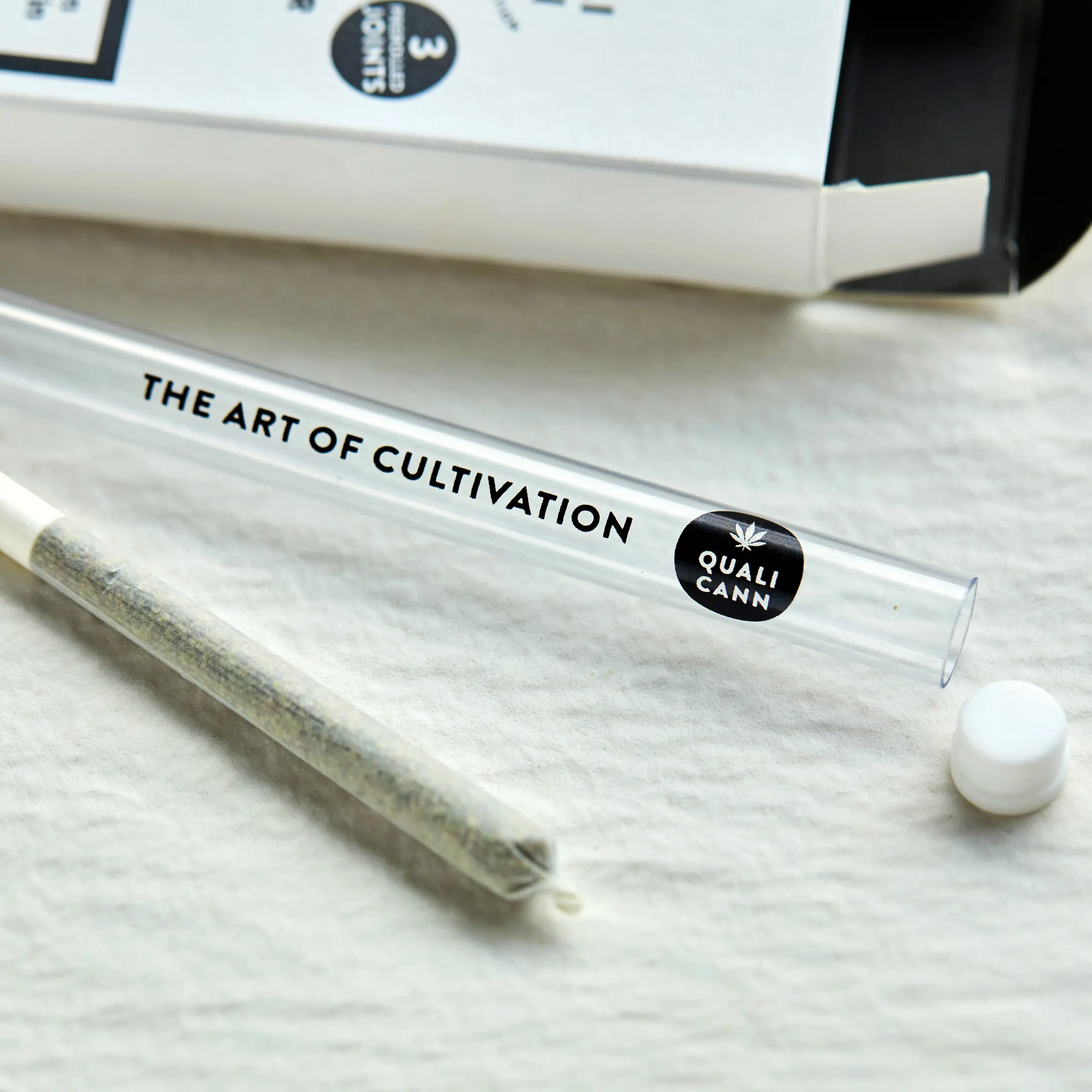 Nahaufnahme eines CBD-Pre-Rolls von Qualicann neben einer transparenten Glasröhre mit der Aufschrift “The Art of Cultivation” – hochwertiges, stilvolles Packaging für Premium-CBD-Produkte.