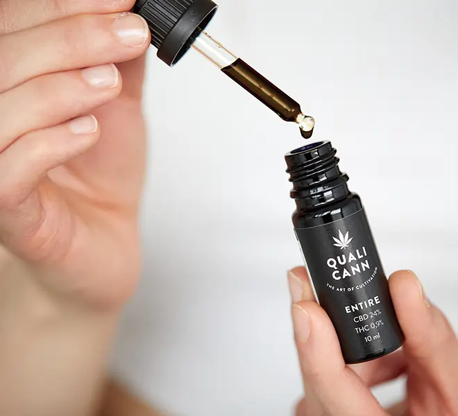 Hand hält QUALICANN ENTIRE CBD-Öl 24% mit THC 0.9 %, während eine Pipette das dunkel gefärbte Vollspektrumöl entnimmt – hochwertiges Schweizer Vollspektrum CBD Öl