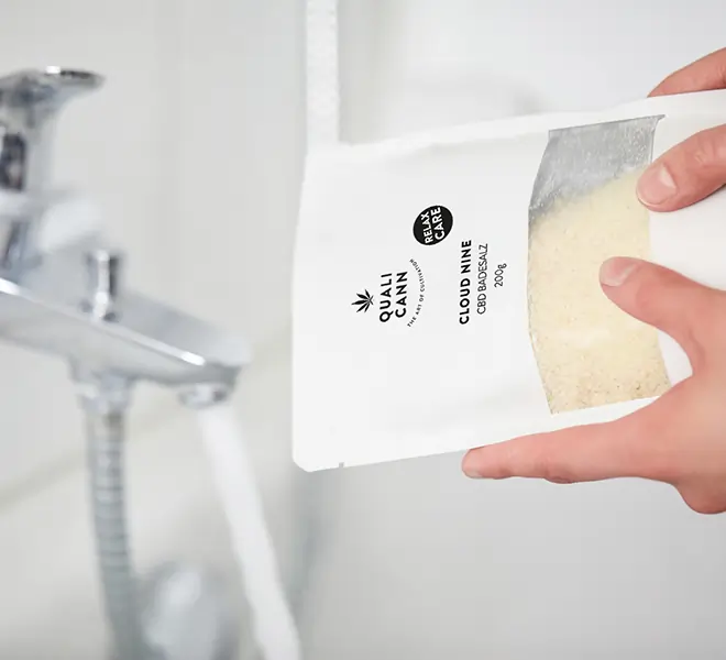 Person füllt Qualicann Cloud Nine CBD-Badesalz in die Badewanne – steht für natürliche Entspannung, Pflege und wohltuende CBD-Wellnessmomente.