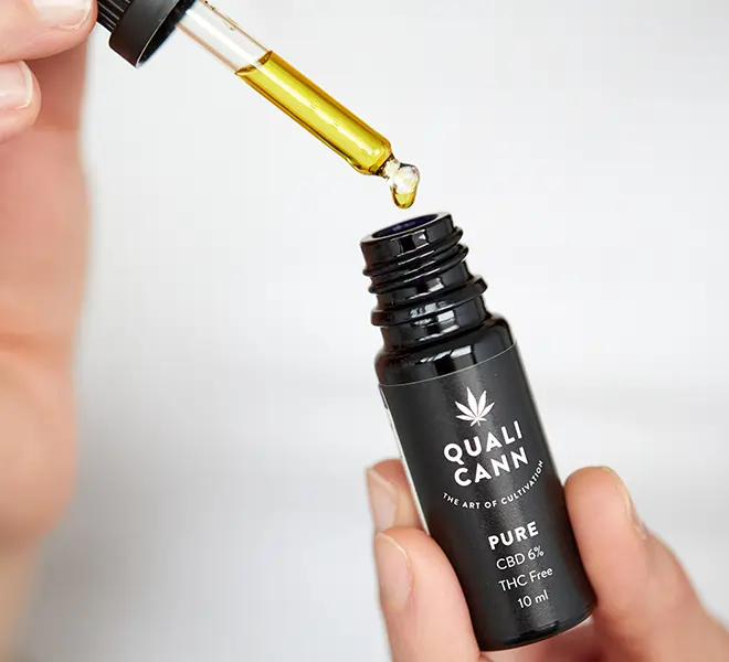 Hand hält QUALICANN PURE CBD-Öl 6% THC-frei, während eine Pipette goldgelbes CBD-Isolatöl entnimmt – hochwertiges Schweizer CBD Öl
