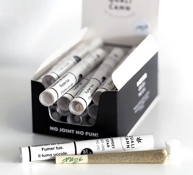Box mit mehreren Qualicann CBD-Pre-Rolls in weißen Röhrchen, ergänzt durch einen einzelnen fertigen Joint im Vordergrund – stilvolles Premium-CBD-Produkt mit PURIZE-Filter für höchsten Genuss.