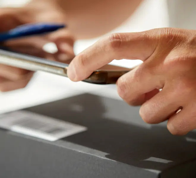 Mitarbeiter verwendet ein Handy, um einen Strichcode auf einer schwarzen Verpackung zu scannen. Dieser wird benötigt für die Versands-Verfolgung.