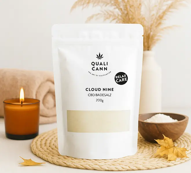 Qualicann Cloud Nine CBD-Badesalz im weissen Standbeutel, dekorativ arrangiert mit Kerze, Handtuch und Naturdeko – Wellness-Produkt für ein entspannendes Badritual.