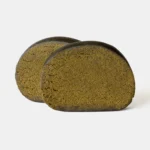 Zwei halbierte, ovale CBD Hash Stücke in braun-grüner Farbe mit feiner, kompakter Struktur auf hellem Hintergrund