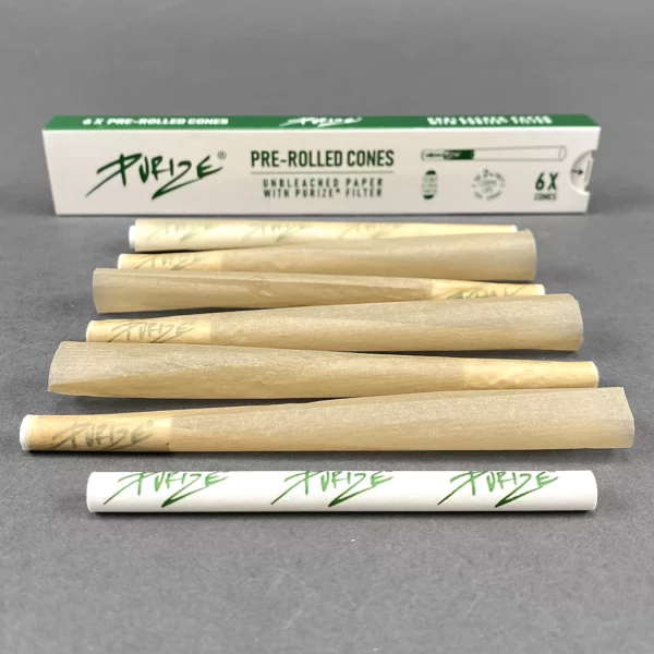 Sechs ungefüllte, vorgerollte Cones aus ungebleichtem Papier mit Purize-Filter, auf grauem Hintergrund arrangiert. Im Hintergrund befindet sich eine grüne Verpackung mit der Aufschrift „Purize Pre-Rolled Cones“